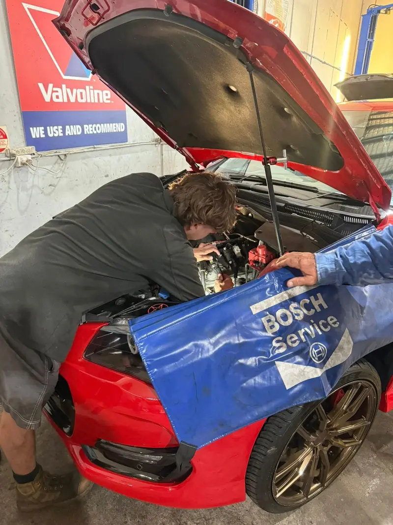 Technician working in the engine bay of a red car