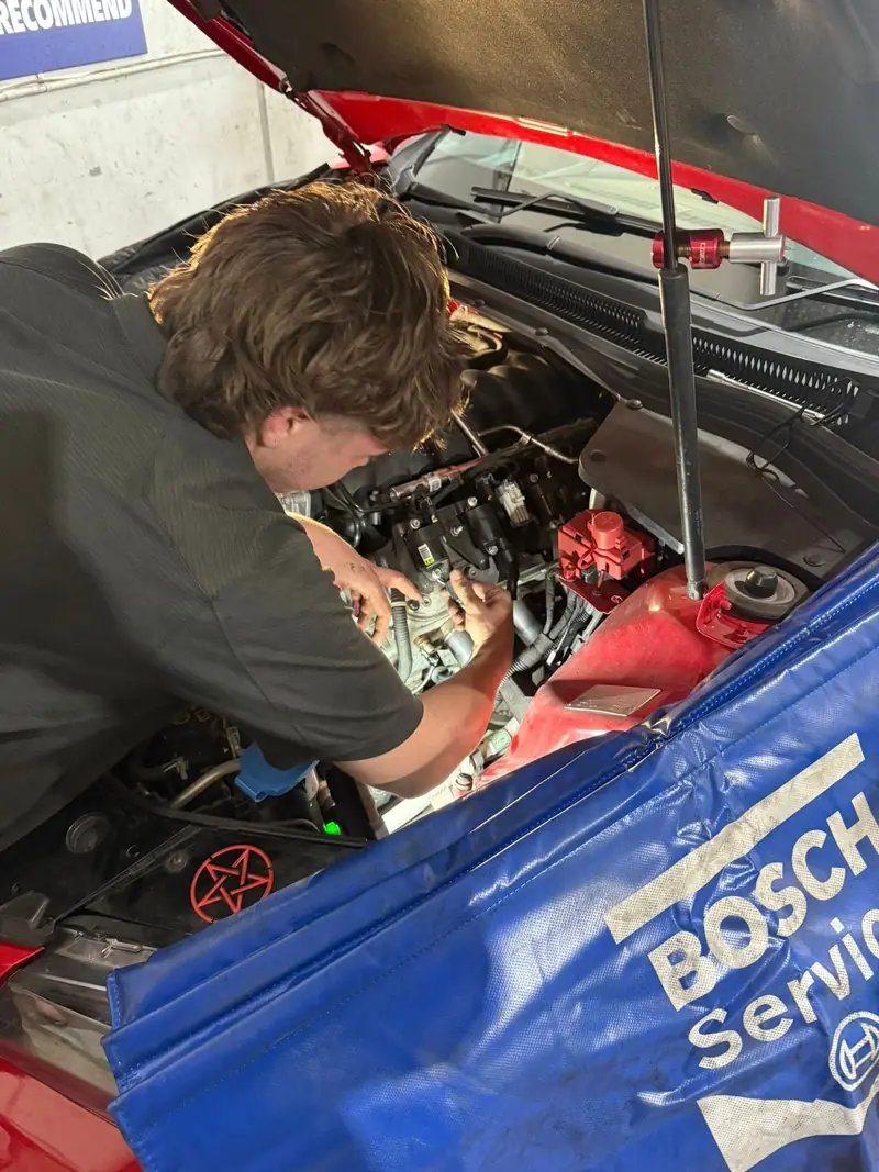 Technician carrying out auto-electrical wiring repairs in an engine bay